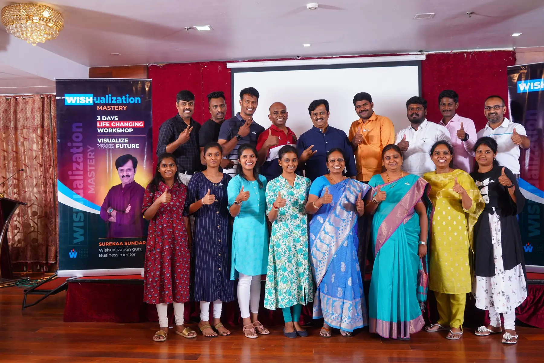WISHualization பேனர்களுக்கு அருகில் கட்டைவிரலை உயர்த்தும் பங்கேற்பாளர்கள்